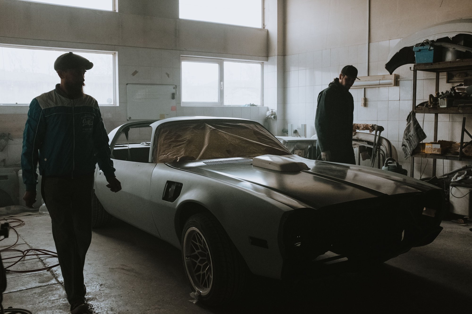 Two mechanics looking over a classic car in a bright workshop