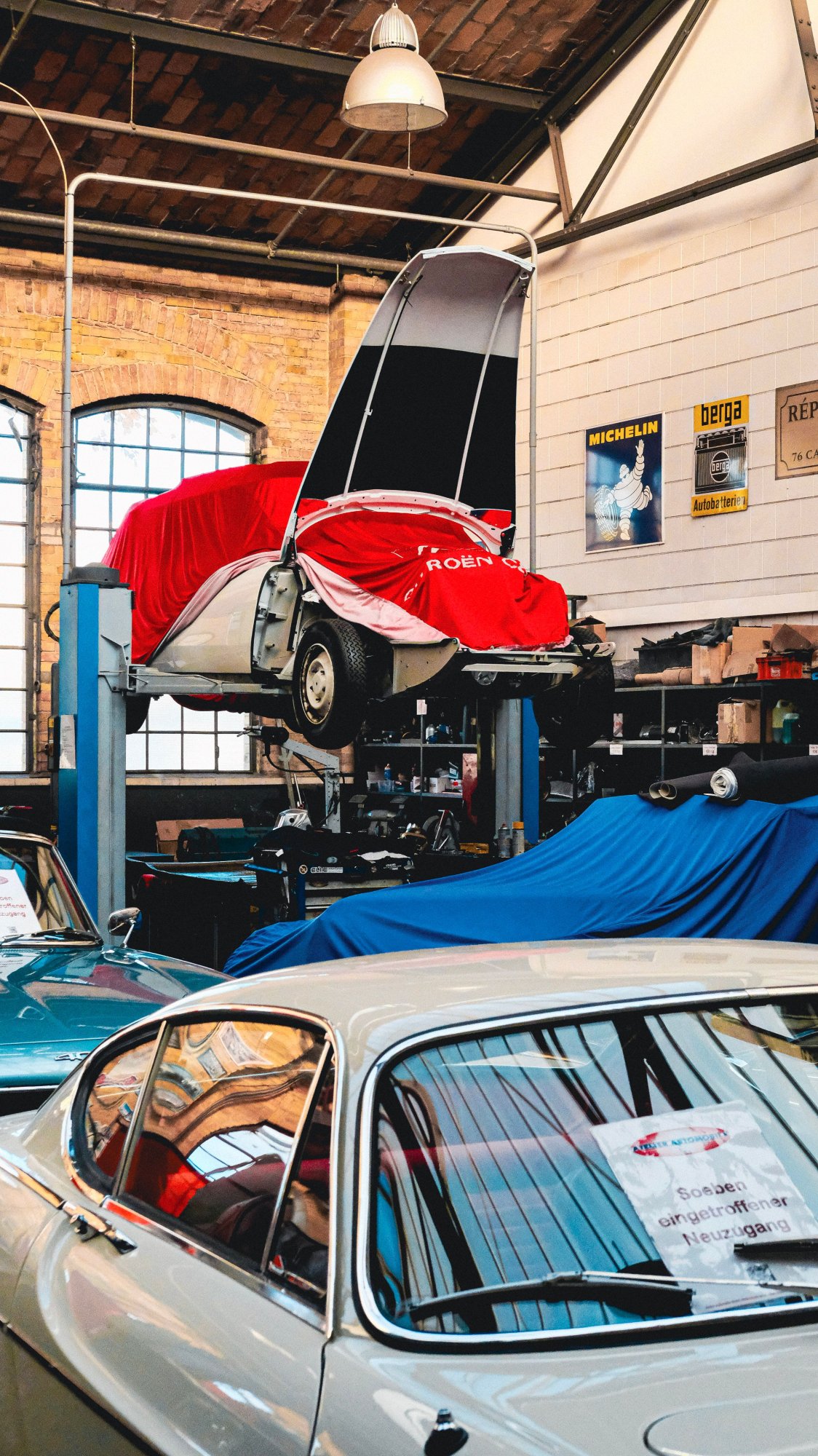 Classic cars on lifts and under covers in a brick-walled garage